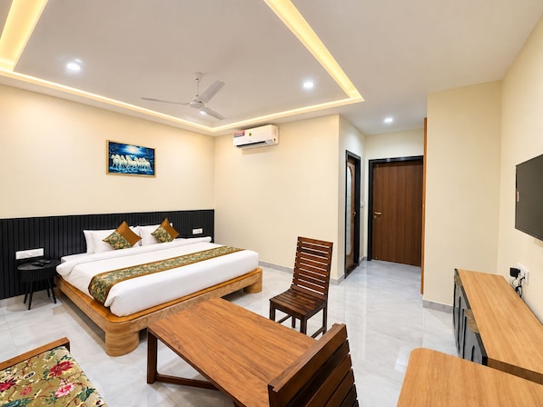 A hotel room with a bed, a desk, a chair, a TV, and a ceiling fan. - Hotel BM Residency (Phalodi)