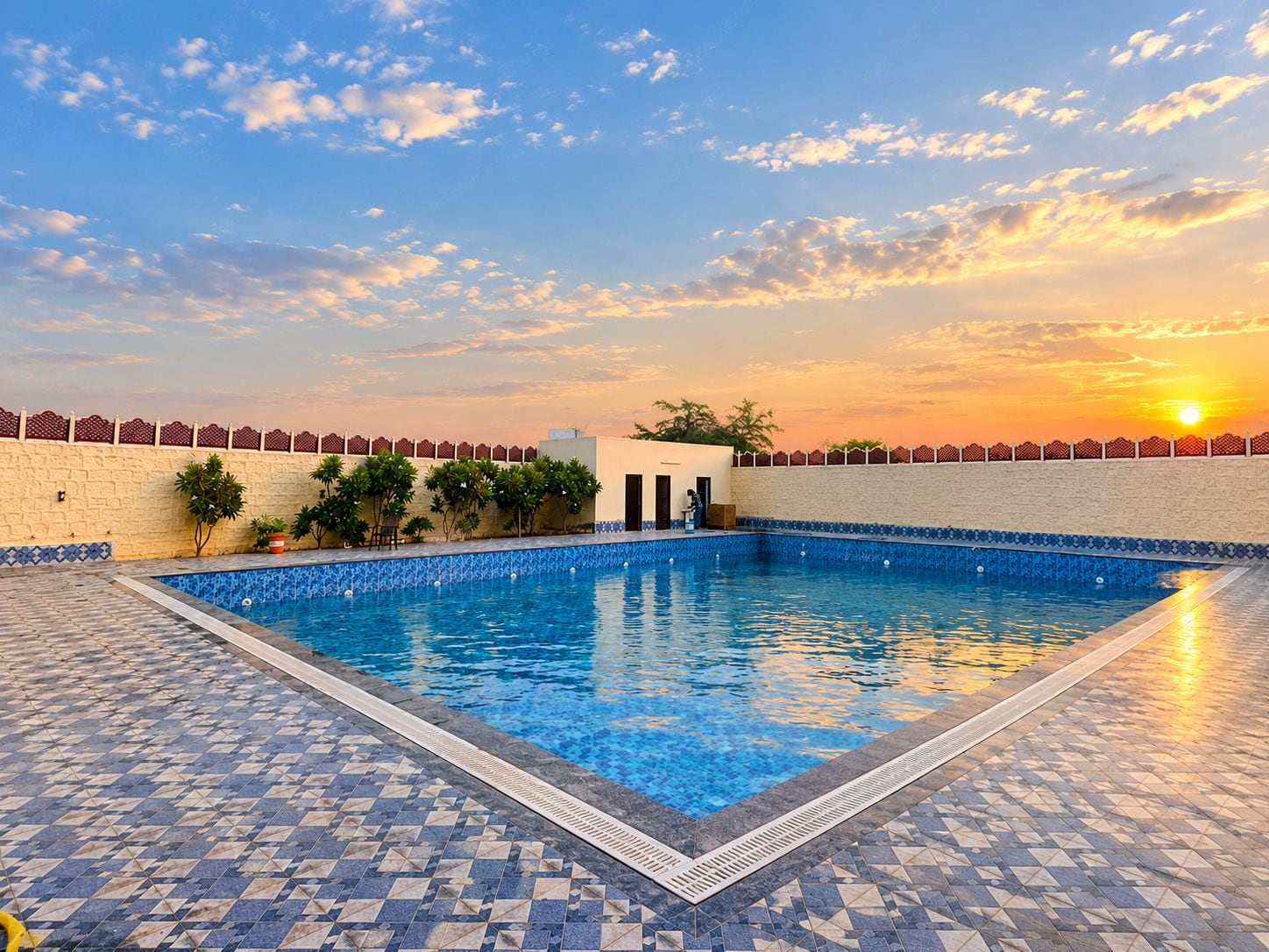 Una piscina con borde de azulejos, rodeada por un muro bajo con una cerca decorativa.