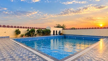 Una piscina con borde de azulejos, rodeada por un muro bajo con una cerca decorativa.