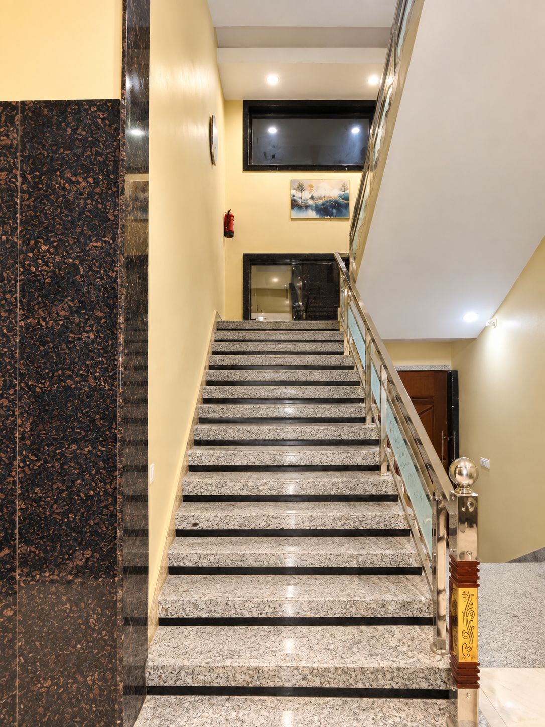 A staircase with a handrail, a fire extinguisher on the wall, and a painting above the door.