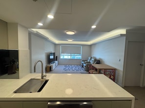 A modern kitchen with a built-in sink, a dining area with a table and chairs, a seating area with a sofa, and a television. - 1 Bdrm Apart 45 sqm-2min walk to Train Stat Free Carpark- Option1 / Option2 Bdrm (Chatswood)