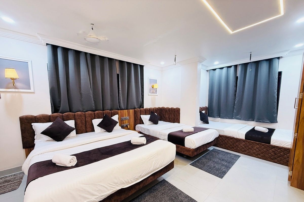 Une chambre d’hôtel avec deux lits, une grande fenêtre avec des rideaux, une tête de lit et une lampe fixée au mur.
