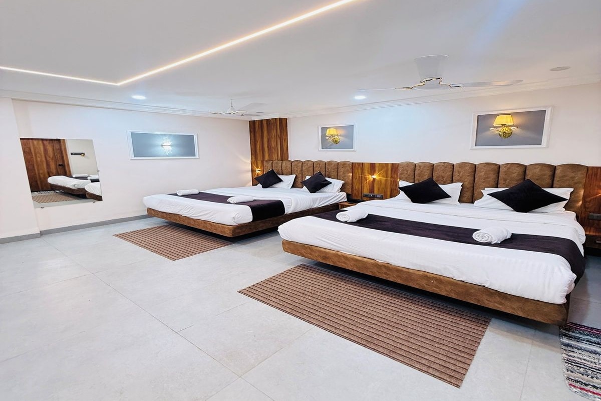 Une chambre d’hôtel avec deux lits, une tête de lit en bois, un miroir et un luminaire au plafond.