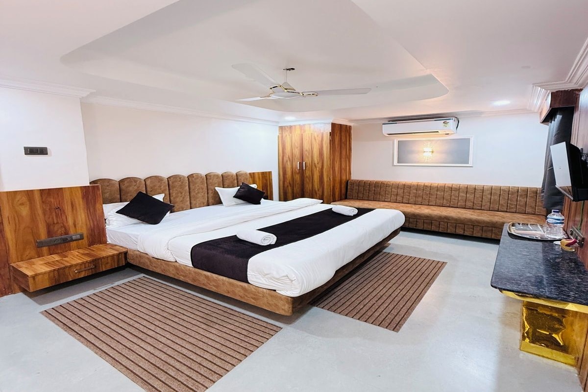 Une chambre moderne avec un grand lit, une tête de lit en bois, un banc et un téléviseur à écran plat.
