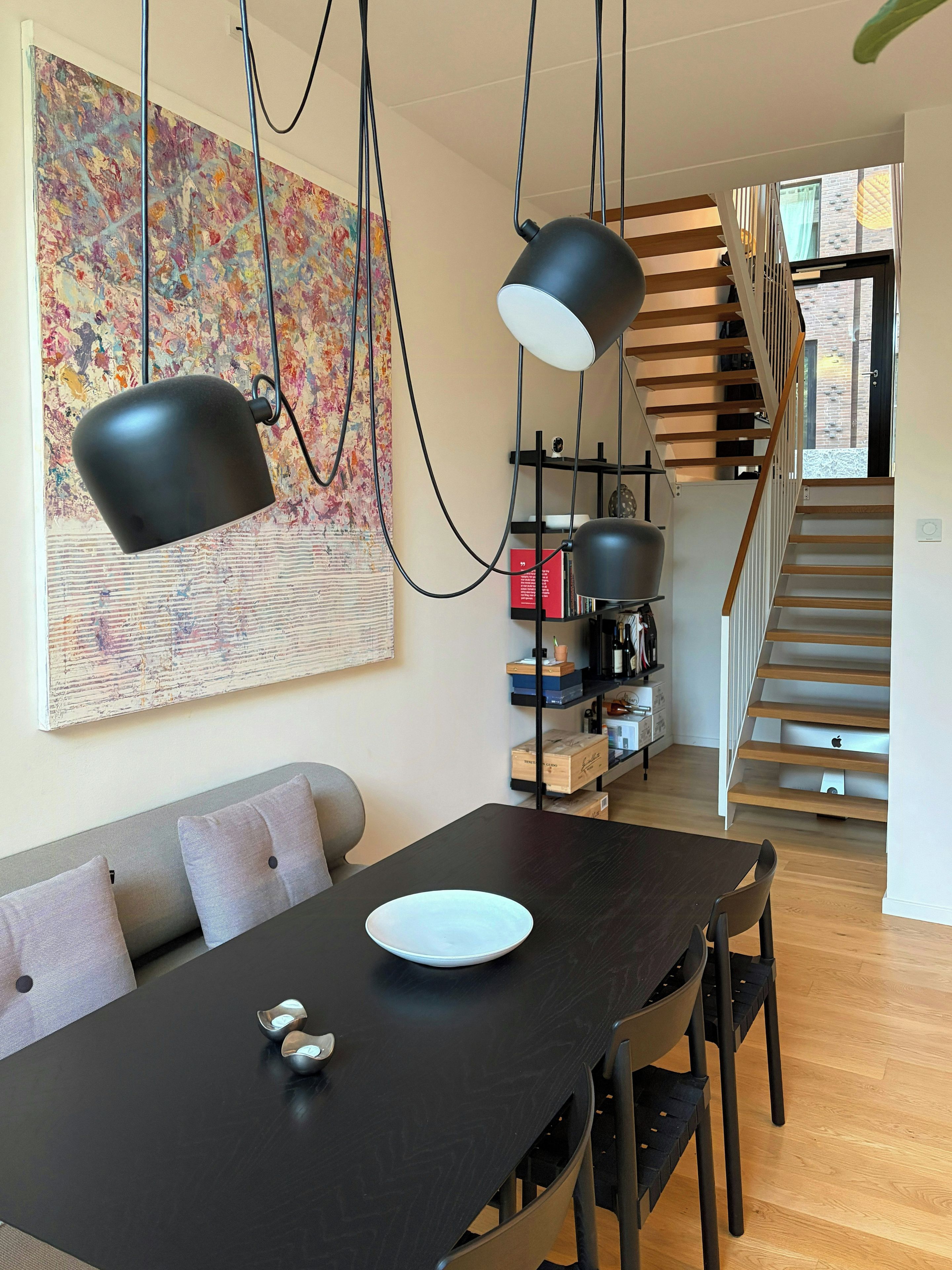 A dining area with a black table, two chairs, a white plate, and two black pendant lights.