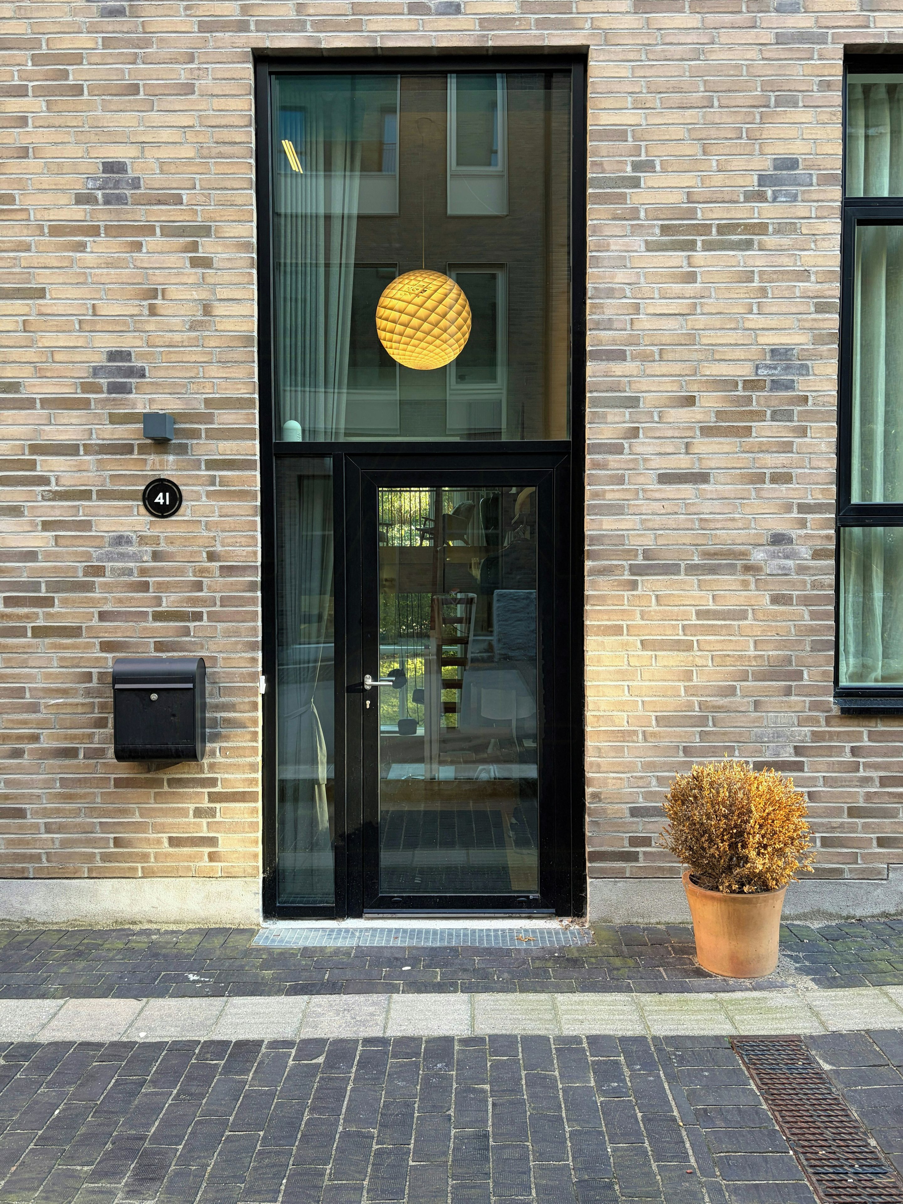 A brick building with a black-framed glass door, a mailbox, and a potted plant on the ground.