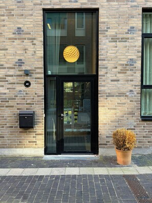 A brick building with a black-framed glass door, a mailbox, and a potted plant on the ground. - Two-storey flat by Carlsberg's garden (København)