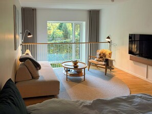 A modern living room with a sofa, a round coffee table, a chair, and a television mounted on the wall. - Two-storey flat by Carlsberg's garden (København)