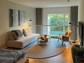 A modern living room with a sofa, armchair, coffee table, and a large window with a view of greenery. - Two-storey flat by Carlsberg's garden (København)