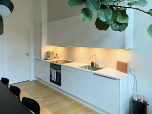 A modern kitchen with white cabinetry, a stainless steel sink, and a built-in dishwasher. - Two-storey flat by Carlsberg's garden (København)