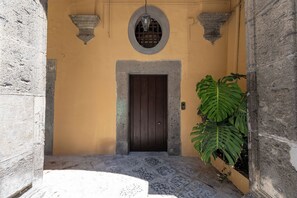 A building entrance with a dark wooden door, a stone archway, and a potted plant. - Living Filomarino (Naples)