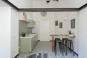 A compact kitchen with a dining area, featuring a tiled floor, a clock, and a small bar area with stools. - Living Filomarino (Naples)