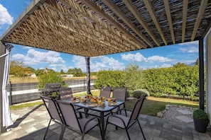 An outdoor patio with a table set for breakfast, surrounded by chairs, under a pergola. - Villa Blue Lagoon (Krsan)