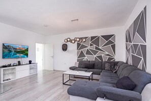 A modern living room with a flat-screen TV, a grey sofa, a coffee table, and a geometric wall design. - Villa Blue Lagoon (Krsan)