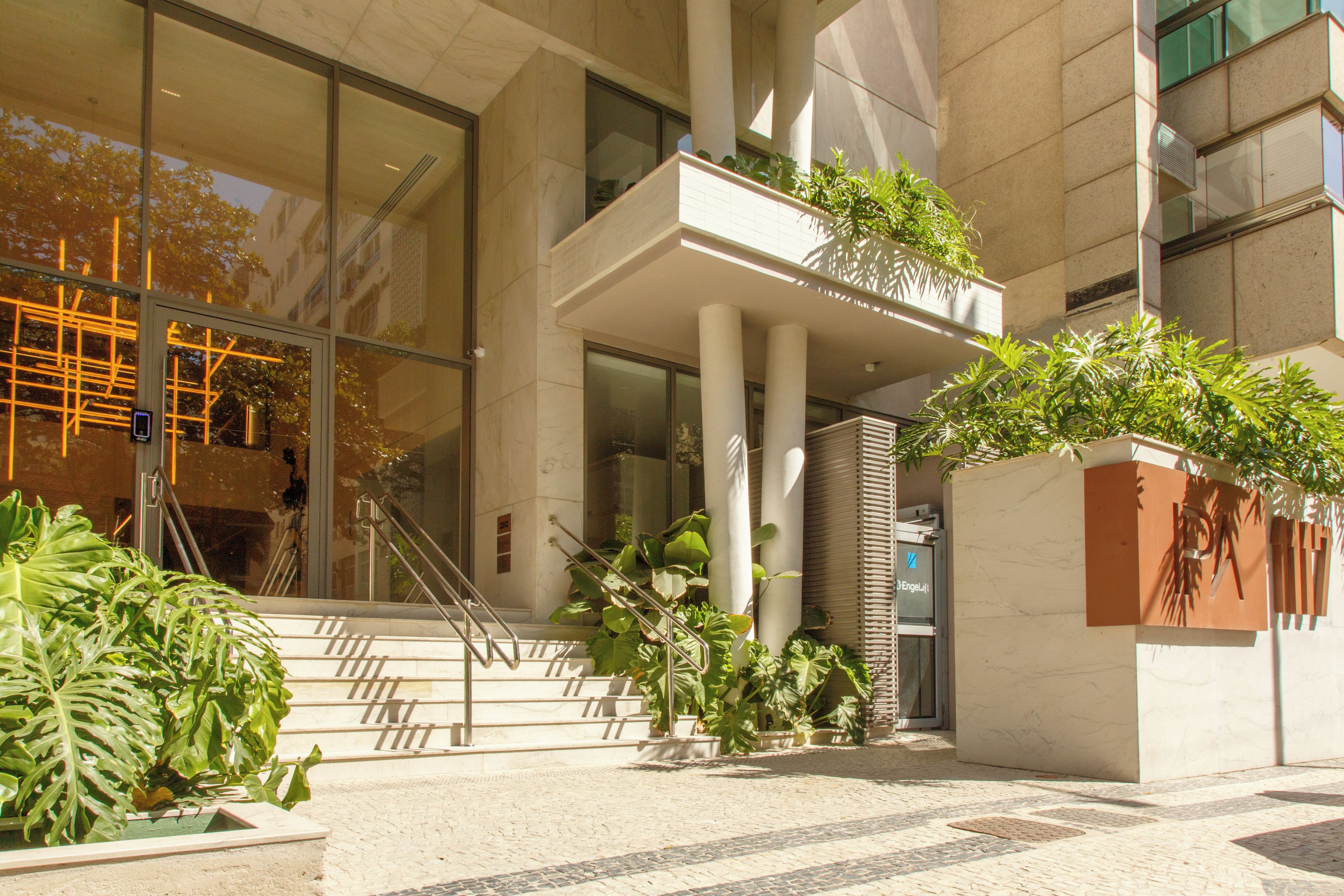A modern building entrance with a glass facade, a set of stairs, and potted plants.