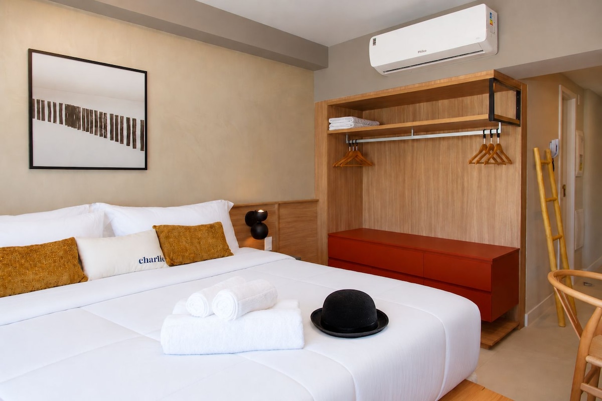 A hotel room with a bed, a red bench, a wardrobe, and an air conditioning unit.