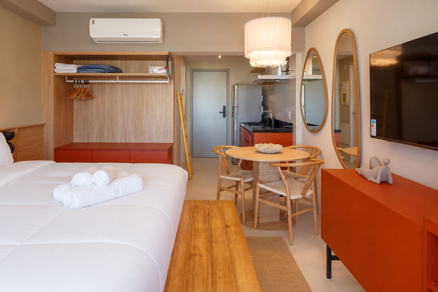 Habitación de hotel con cama, armario de madera, mesa de comedor con sillas, espejo y televisión.