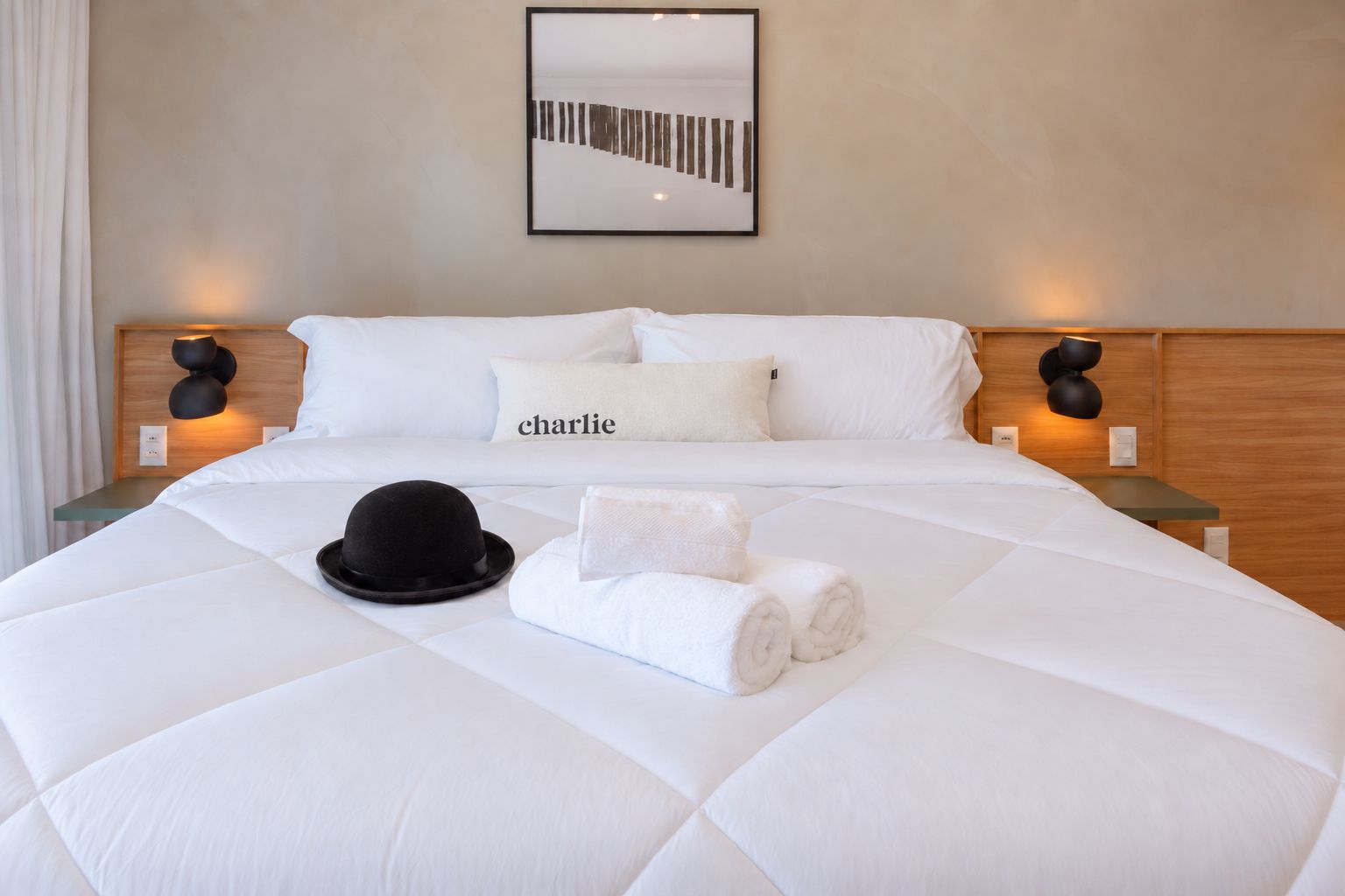 A hotel room with a large bed, two bedside tables, a wall-mounted picture, and a name pillow.