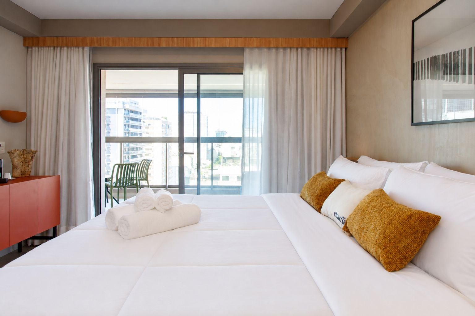 A hotel room with a large bed, a desk, a chair, and a view of the city through the window.