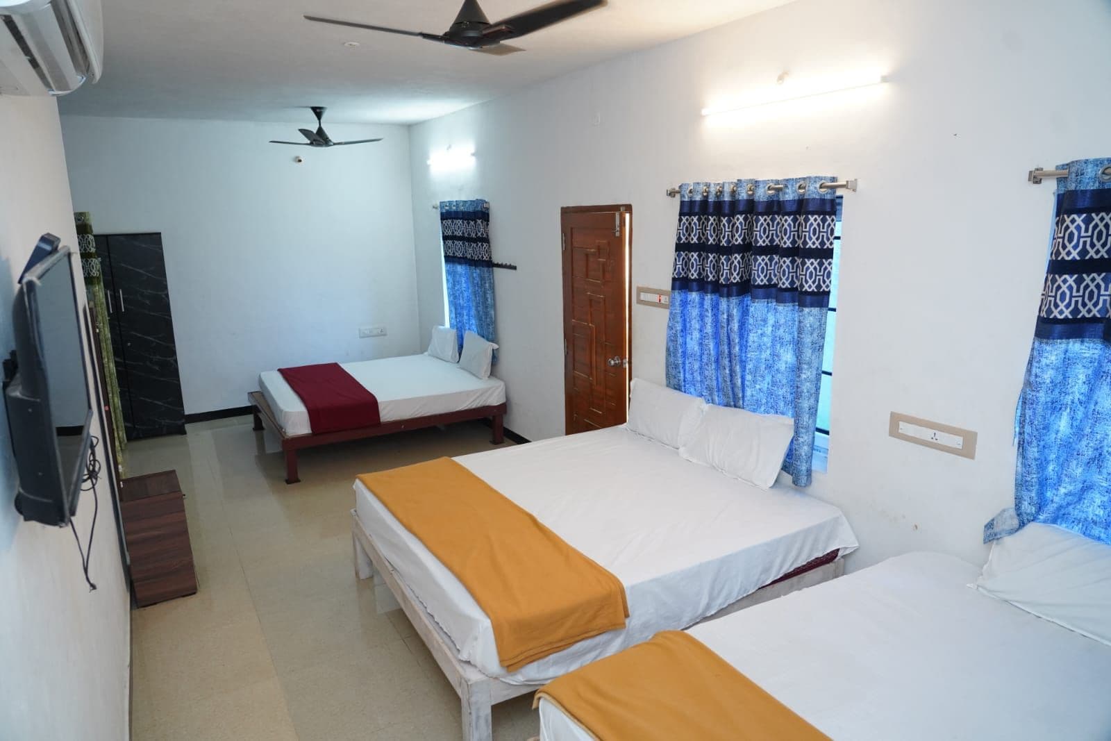 Una habitación de hotel con dos camas, ventilador de techo, televisión y una puerta.