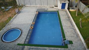 A rectangular swimming pool with a surrounding deck, a smaller circular pool, and a fenced area with palm trees.