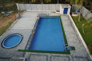 A rectangular swimming pool with a surrounding deck, a smaller circular pool, and a fenced area with palm trees. - REHO RESORT (Rameshwaram)