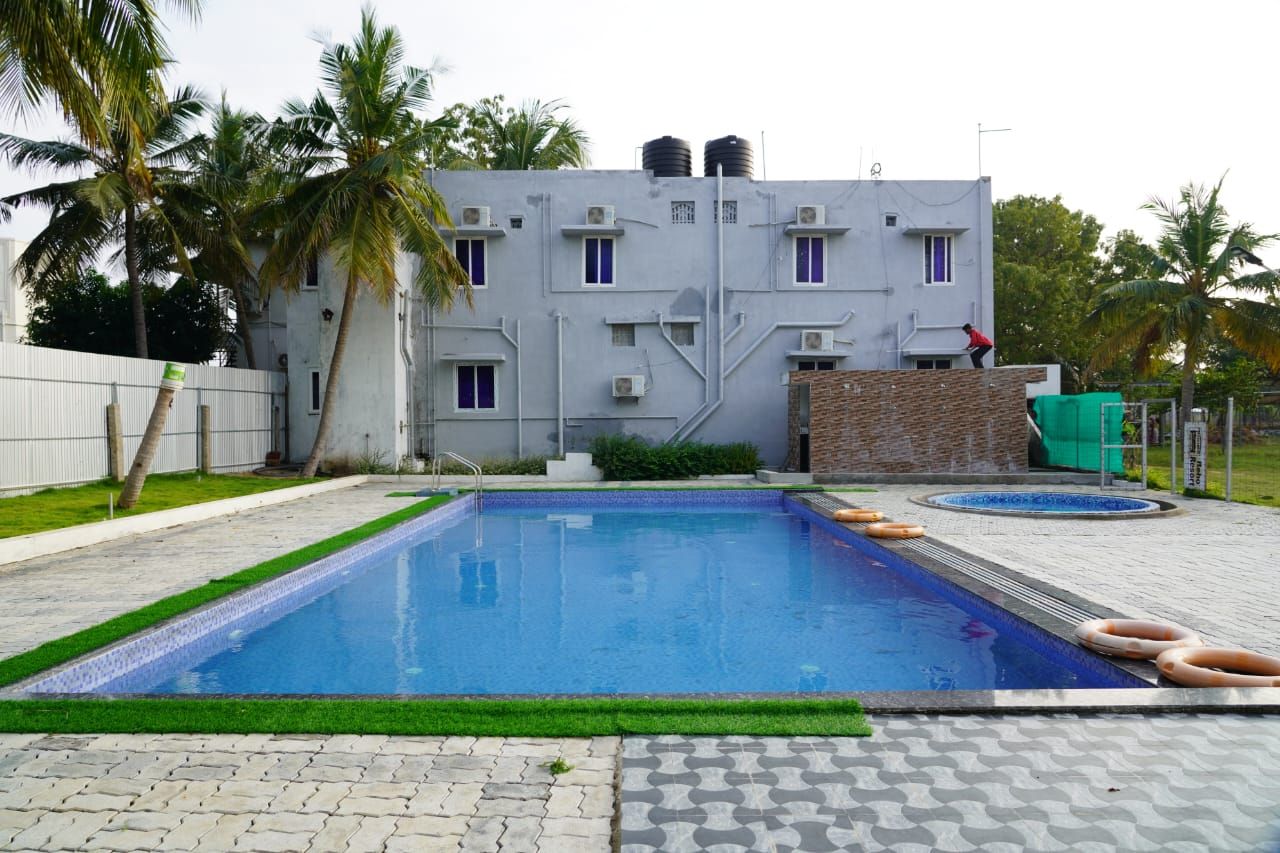 A swimming pool with a tiled deck, a brick wall, and a building with multiple windows and air conditioning units.