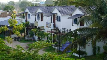 A row of white buildings with tiled roofs and balconies, surrounded by greenery and a parked motorcycle.