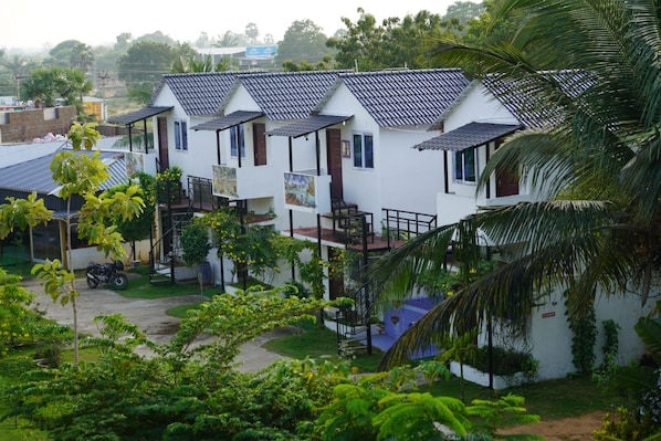 A row of white buildings with tiled roofs and balconies, surrounded by greenery and a parked motorcycle. - REHO RESORT (Rameshwaram)
