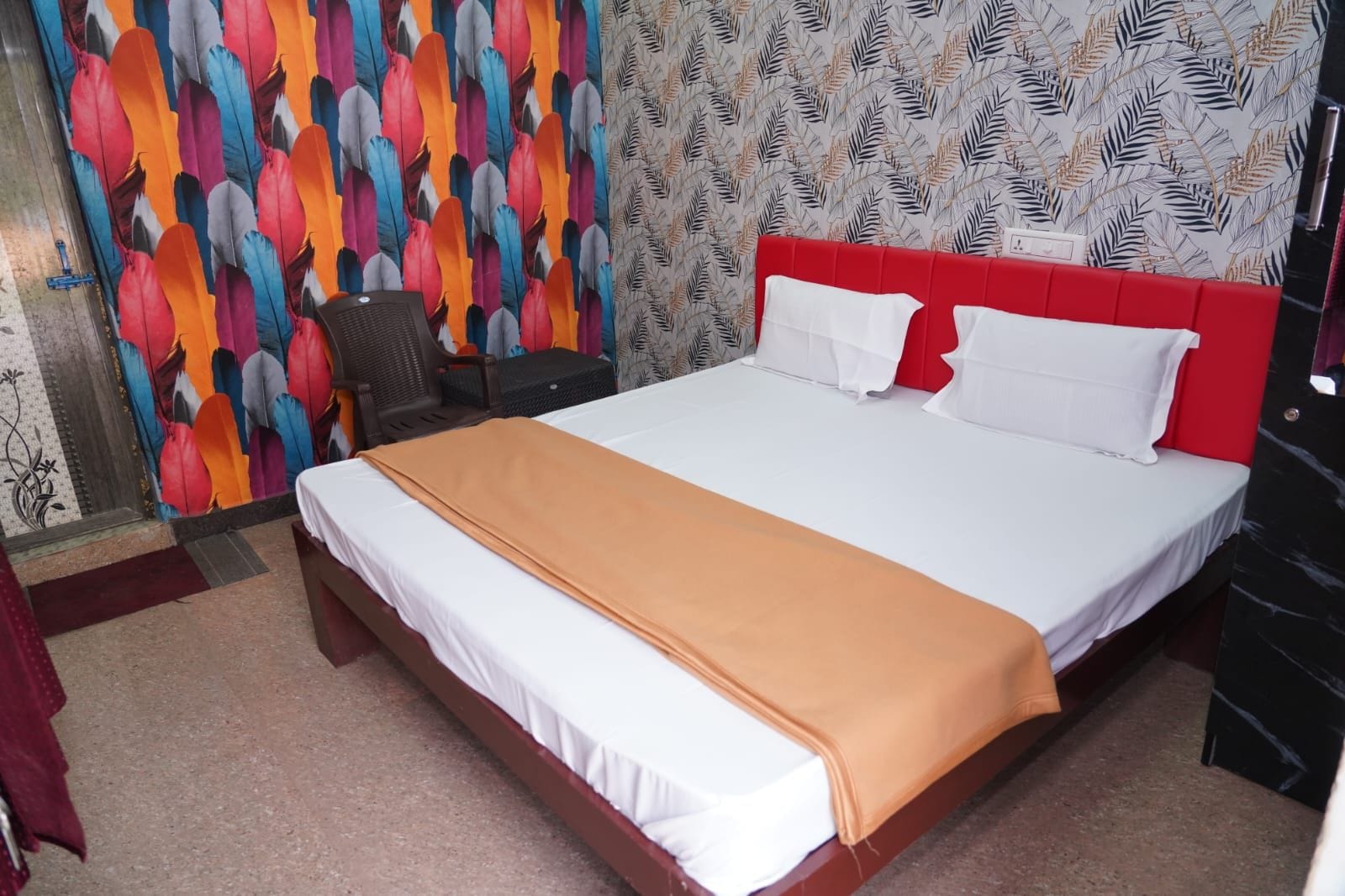 Quarto de hotel com uma cama grande, cabeceira vermelha, parede colorida e papel de parede estampado.