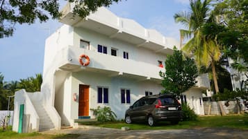 Un edificio de dos pisos con una escalera que conduce a la entrada, un coche estacionado adelante y un flotador salvavidas colgado en la pared exterior.
