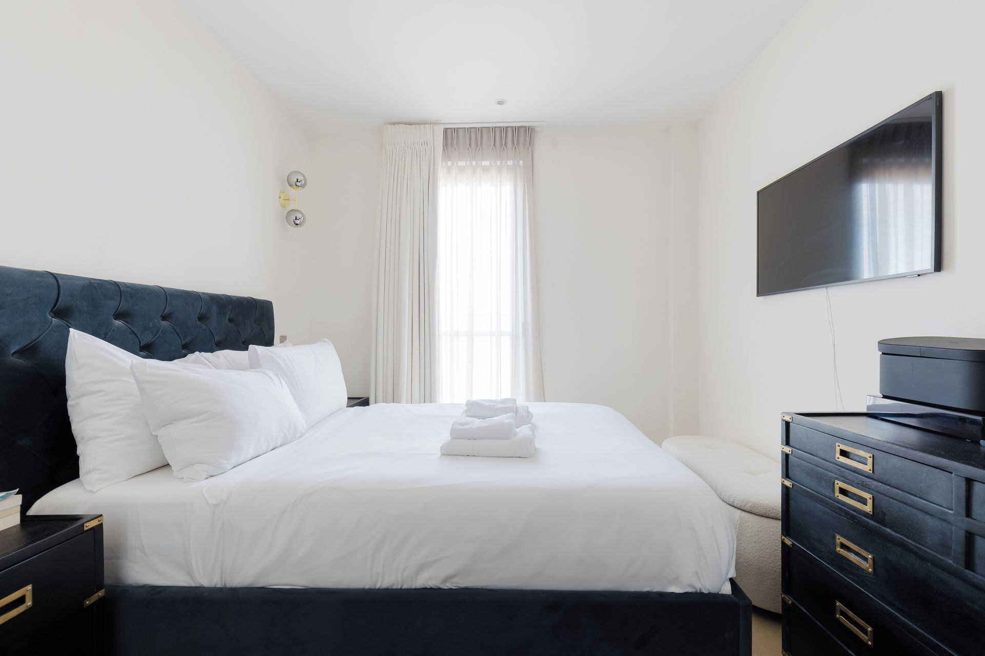 A hotel room with a large bed, a flat-screen TV, a dresser, and a window with curtains.