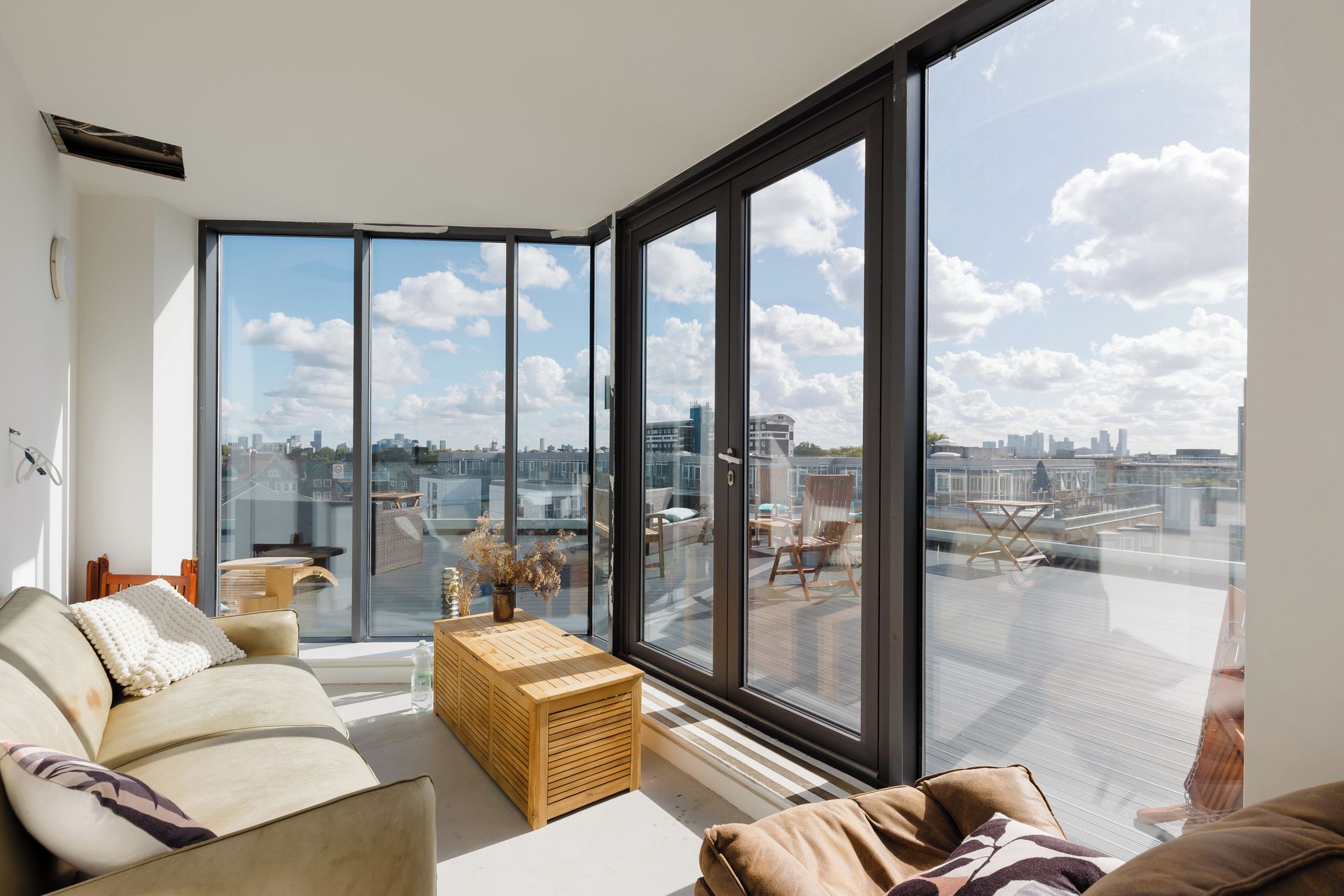 A modern living room with a large glass window, a sofa, a wooden coffee table, and a view of the cityscape.