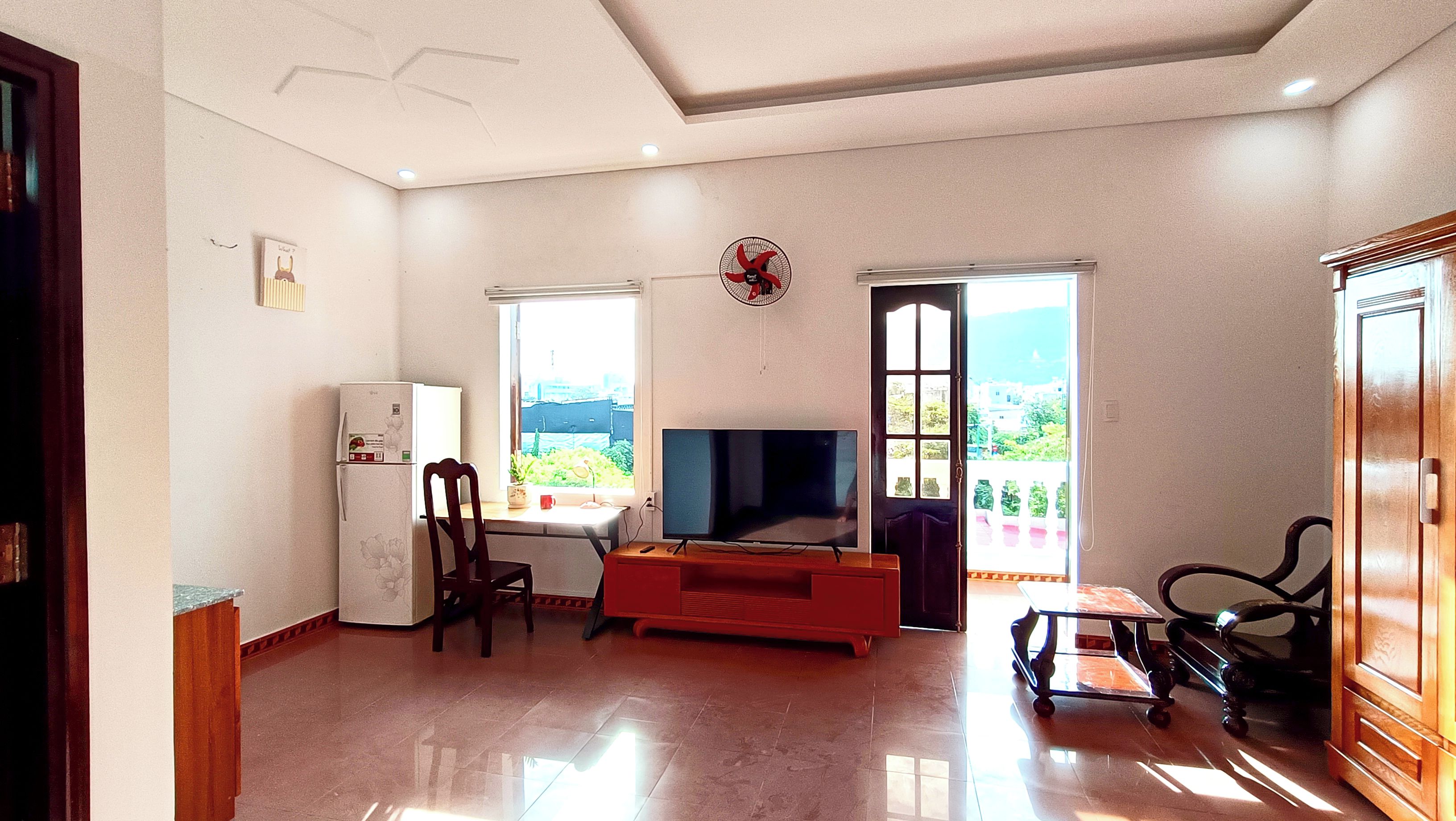 Sala de estar com televisão, geladeira, mesa de jantar e vista para o exterior.