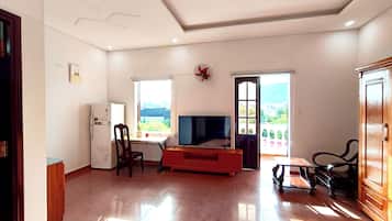 Sala de estar com televisão, geladeira, mesa de jantar e vista para o exterior.