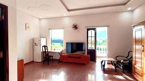 Sala de estar com televisão, geladeira, mesa de jantar e vista para o exterior.