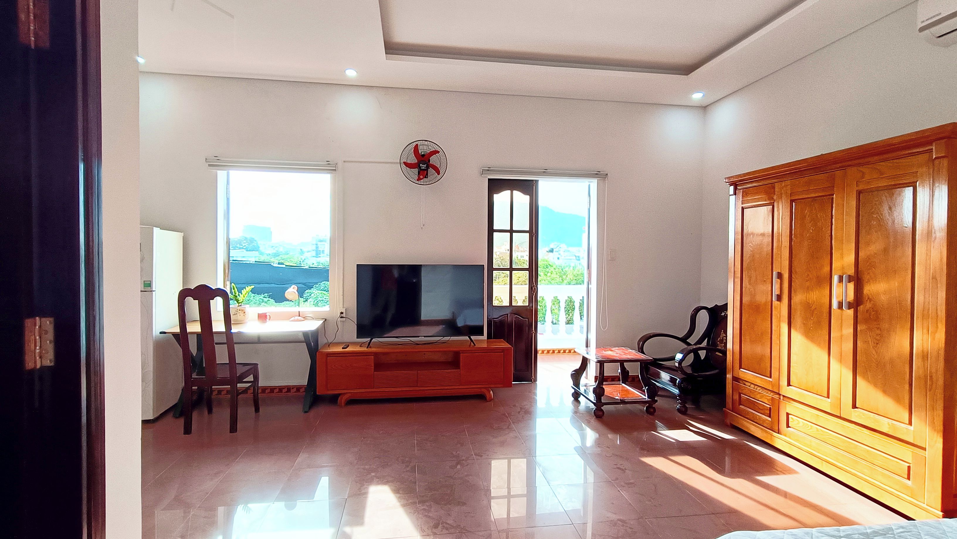 A living room with a TV, wooden furniture, and a view through the windows.
