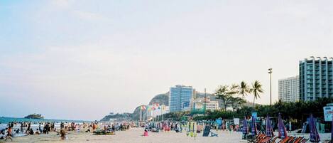 A beach with people, umbrellas, and buildings in the background.