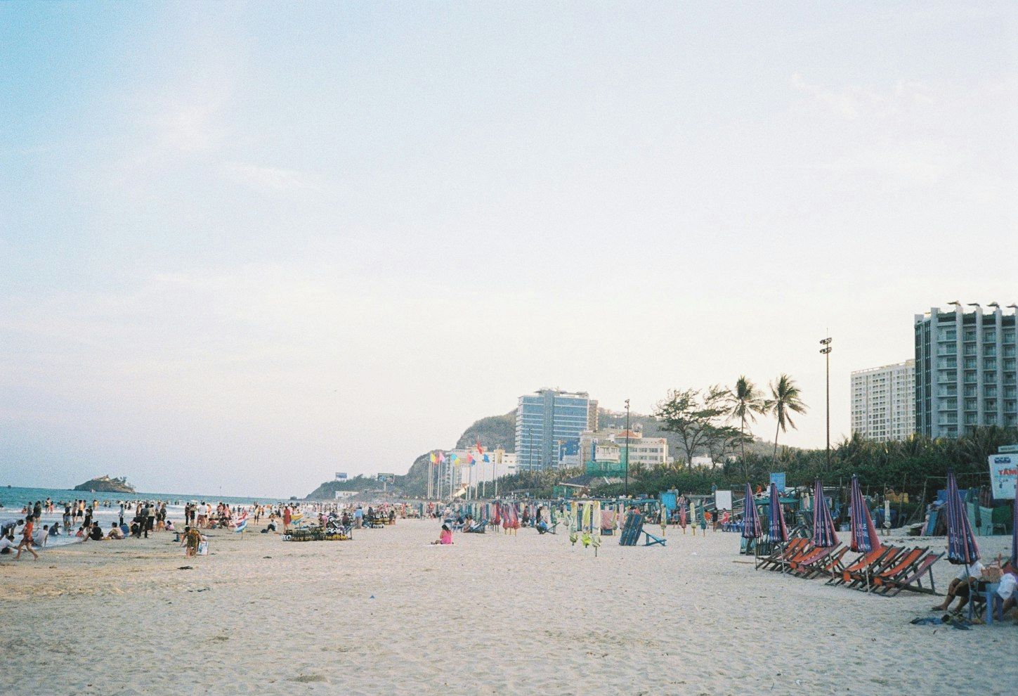 A beach with rows of beach chairs and umbrellas, a sandy shore, and buildings in the background.