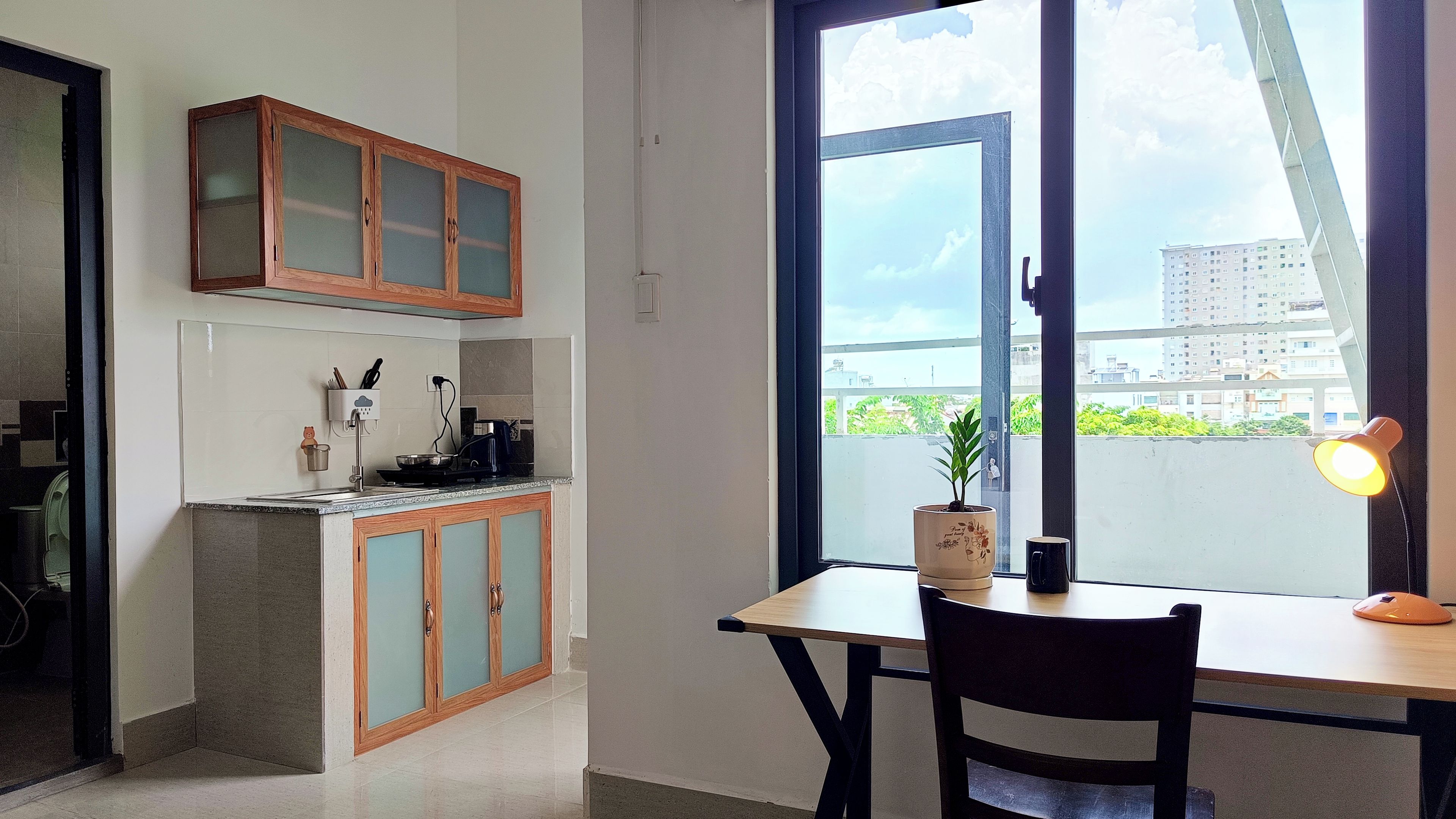 A modern kitchen with a dining area, a large window with a view of buildings, and a potted plant on the table.
