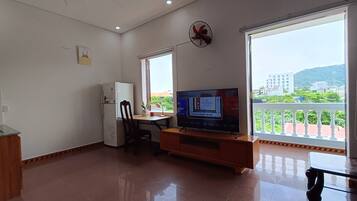 Un espacio habitable compacto con kitchenette, televisor y balcón con vistas a edificios y áreas verdes.