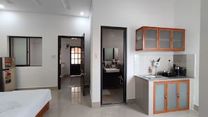 A hotel room with a bed, a kitchenette, a bathroom, and a door leading to another room.