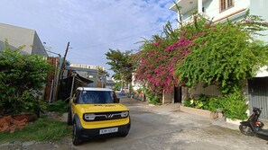 A narrow street with a yellow vehicle parked on the side, surrounded by greenery and buildings.