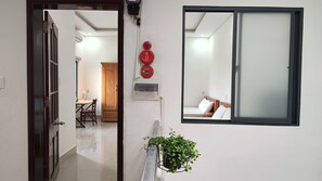 A hallway leading to a bedroom with a bed, a window, and a potted plant.