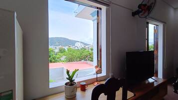 Una habitación con un ventanal grande, un televisor sobre un mueble, una planta en maceta y una taza roja en el alféizar.