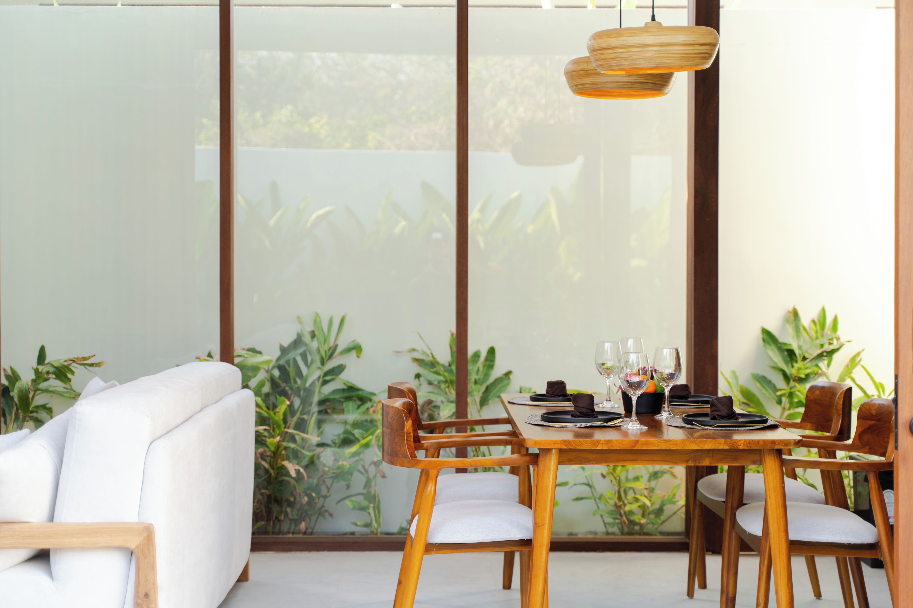A dining area with a table set for two, wooden chairs, and a white sofa.