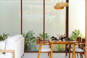 Un comedor con una mesa lista para dos personas, sillas de madera y un sofá blanco.