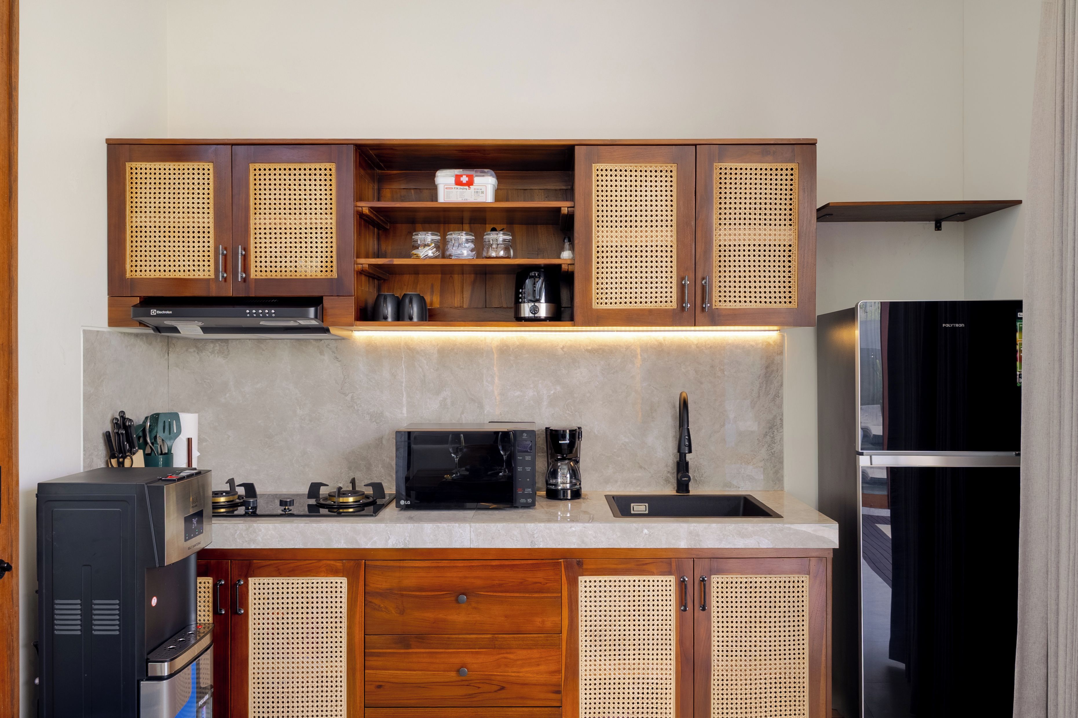 Cocina compacta con armarios de madera, microondas, cafetera y refrigerador.