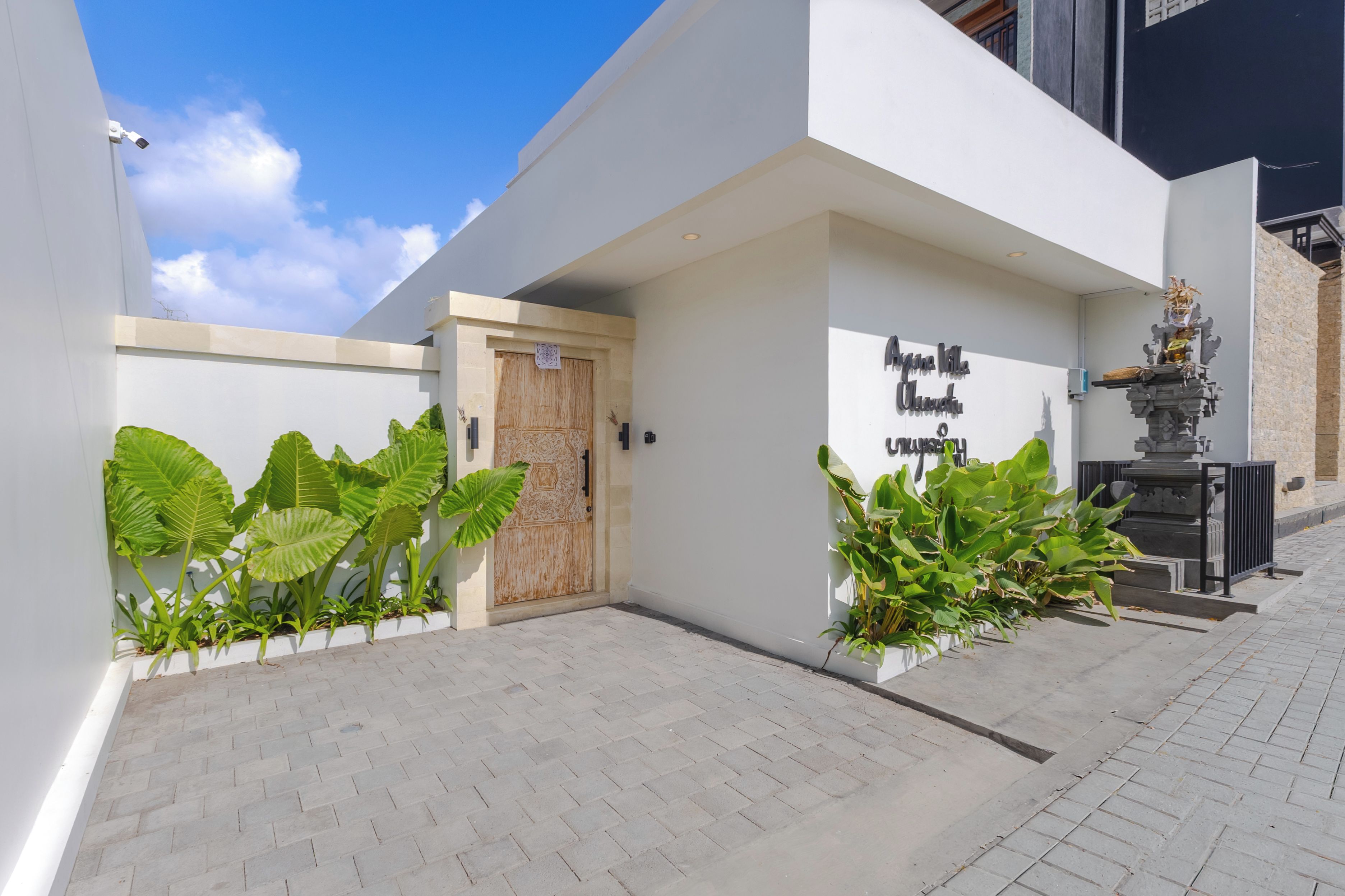 Un edificio moderno con una puerta de madera grande, un letrero con texto y plantas en macetas.