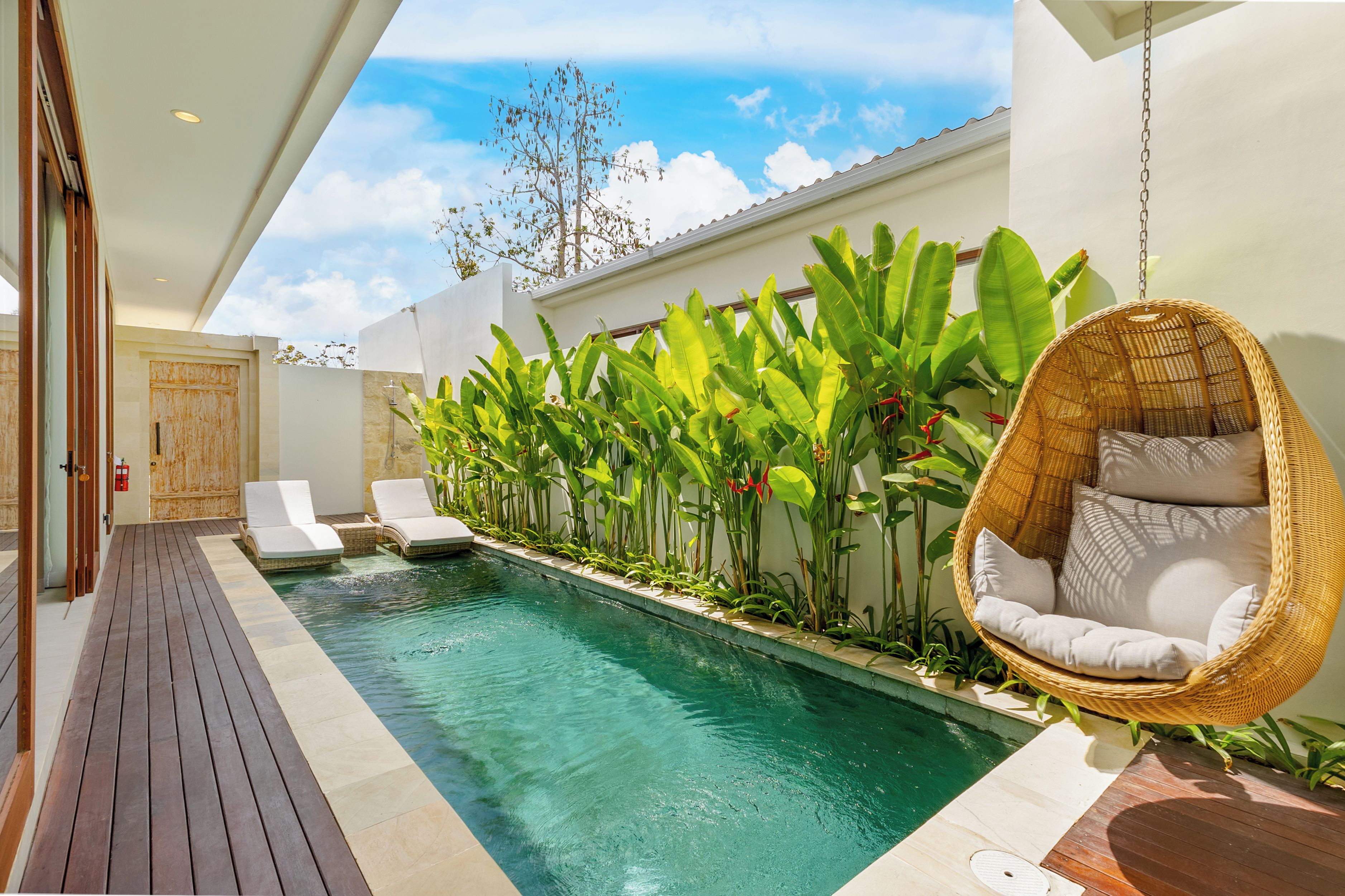 A pool area with a hanging chair, lounge chairs, and tropical plants.